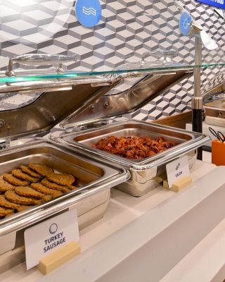 A buffet setup featuring trays of turkey sausage, bacon, and scrambled eggs. Each tray is labeled, and the setup is in a clean, modern design.