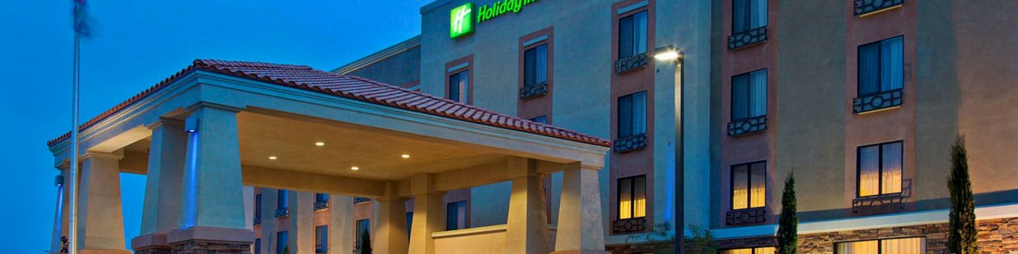 A hotel with a prominent sign reading "Holiday Inn Express & Suites" under evening lighting is visible, showcasing the entrance and surrounding area.