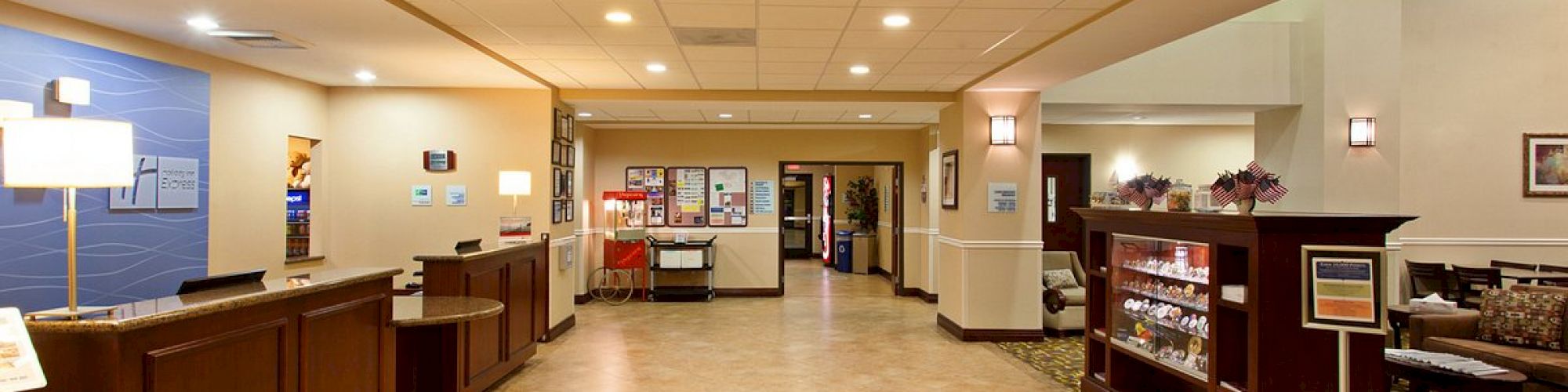 The image shows a spacious lobby with a reception desk on the left, a sitting area on the right, and a corridor at the end.