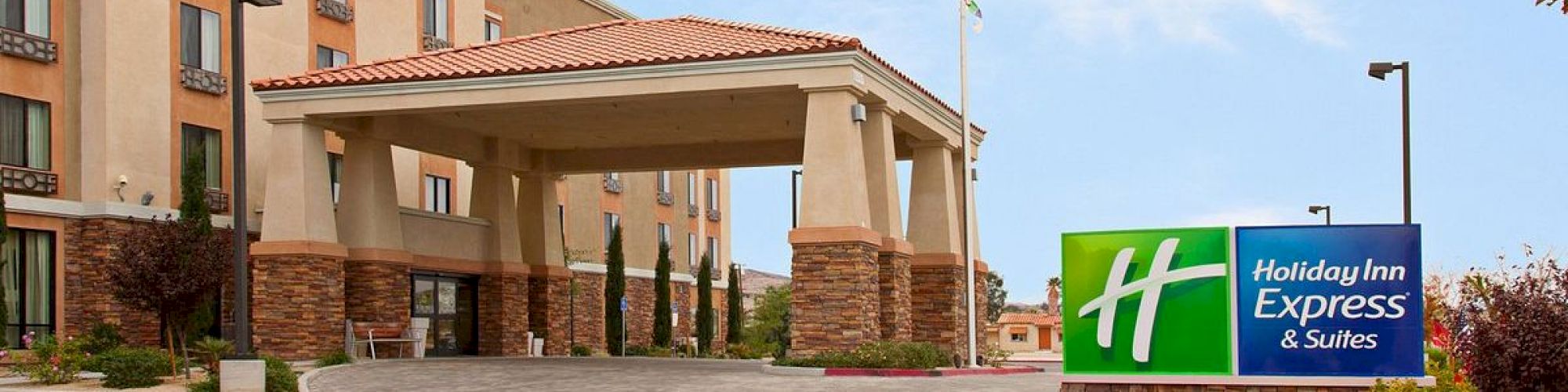 The image shows the exterior of a Holiday Inn Express & Suites hotel with a large entrance, flagpole, and branded signage in the front.