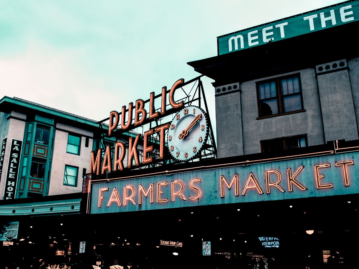 The image shows a public market with neon signs reading "Public Market Center" and "Farmers Market," presumably Pike Place Market in Seattle.