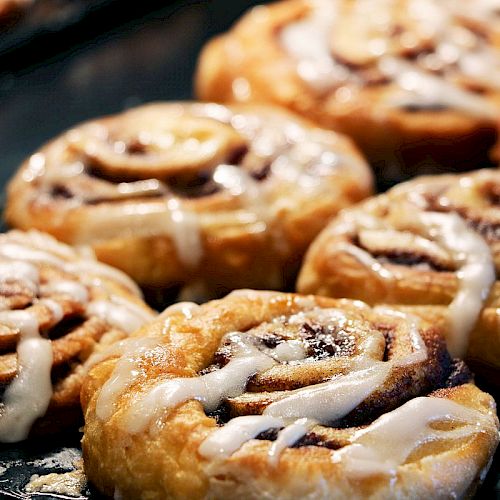 The image shows a tray of freshly baked cinnamon rolls drizzled with icing, placed closely together, and looking delicious.