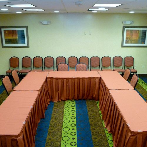 A conference room with a U-shaped table arrangement, red tablecloths, several chairs, and abstract artwork on beige walls.