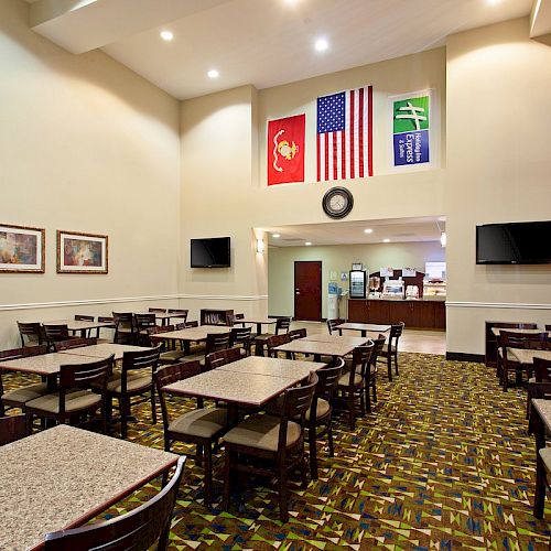 A dining area with tables and chairs, an American flag, and other flags on the wall, a clock, and a counter area in the background.