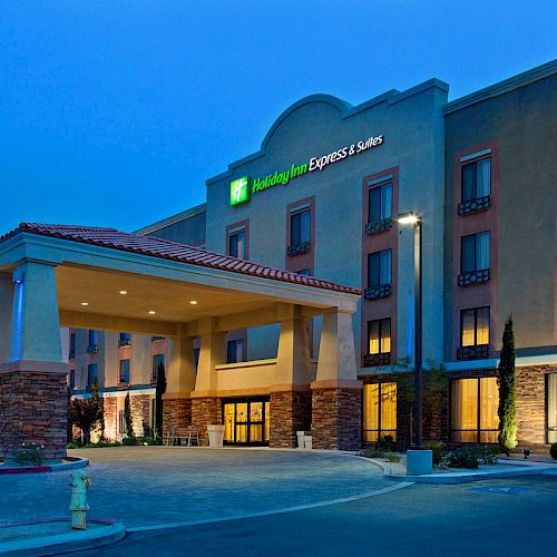 A hotel building with a recognizable logo, featuring a covered entrance area and illuminated windows during the evening.