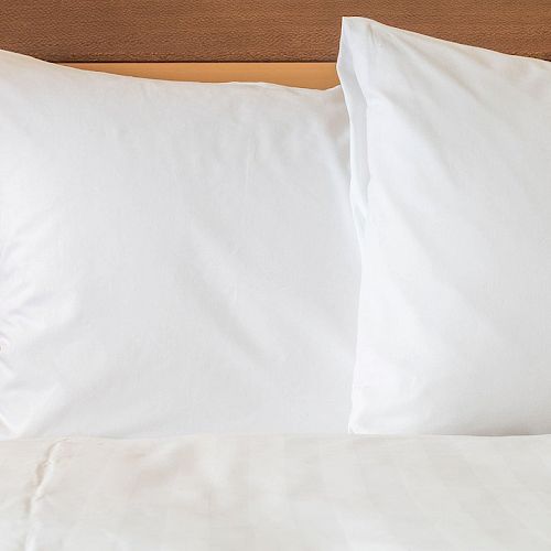 The image shows two white pillows placed side by side on a bed, with a wooden headboard in the background.