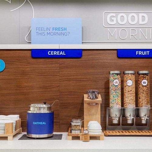 The image shows a breakfast station with cereal, fruit, oatmeal, and breakfast condiments, labeled 