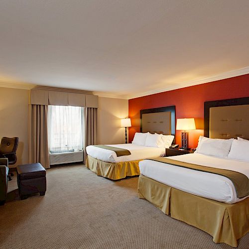 The image shows a hotel room with two large beds, a workstation with a chair, lamps, a TV, and a window with drapes. The room has beige carpet.