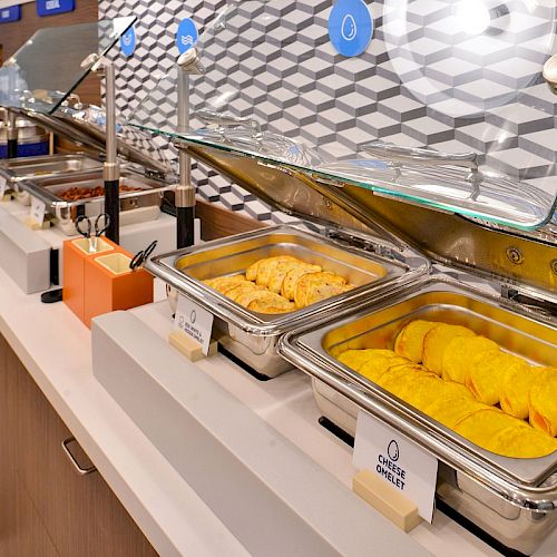 The image shows a buffet with a variety of breakfast foods, including omelettes and pastries, laid out in stainless steel chafing dishes.