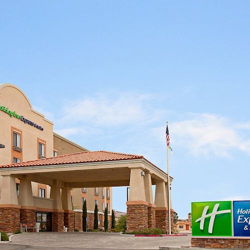 The image shows the exterior of a Holiday Inn Express & Suites hotel with a large blue and green sign near the entrance and a flagpole nearby.