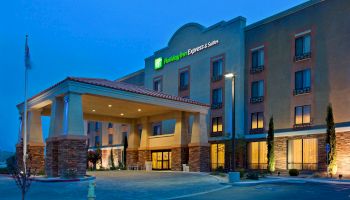 The image shows an illuminated Holiday Inn Express & Suites building at dusk with an entrance canopy and surrounding landscape elements.