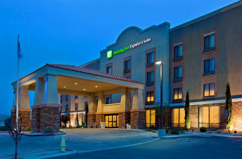 The image shows an illuminated Holiday Inn Express & Suites building at dusk with an entrance canopy and surrounding landscape elements.