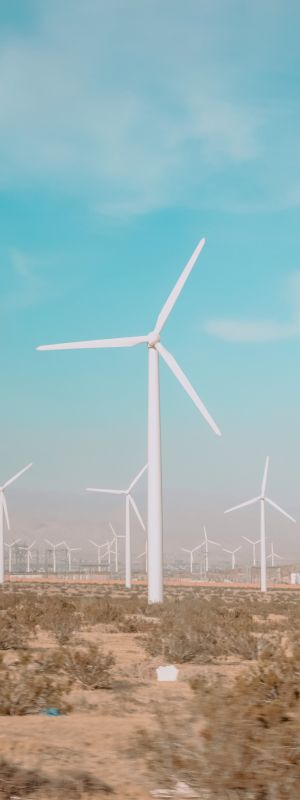 The image shows a landscape with numerous wind turbines installed in a desert area under a clear blue sky, generating renewable energy.